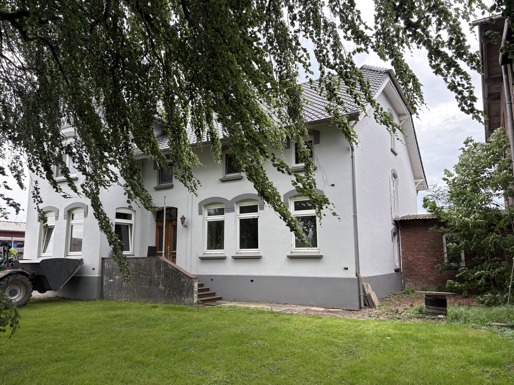 Verputztes Altbauwohnhaus mit grauem Sockel und großem Garten