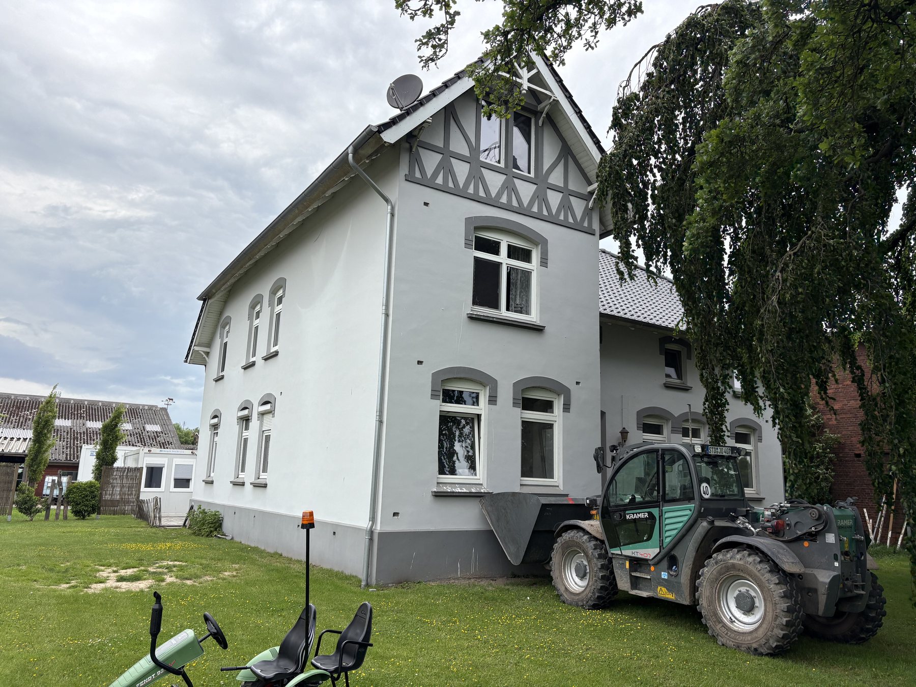 Verputztes Altbauwohnhaus mit Baustellenfahrzeug im Garten